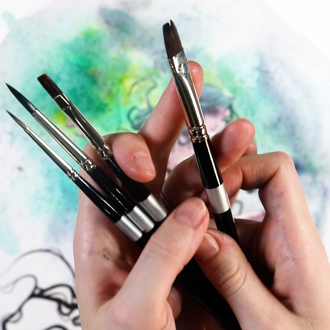 Hands display black-handled brushes above a green-and-blue watercolor painting.