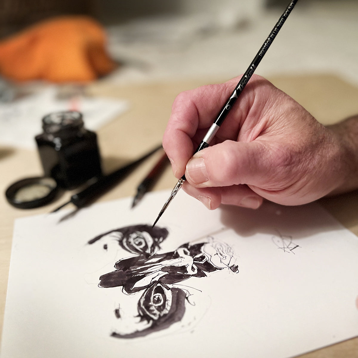Hand paints black details in a symmetrical ink illustration using a fine brush.