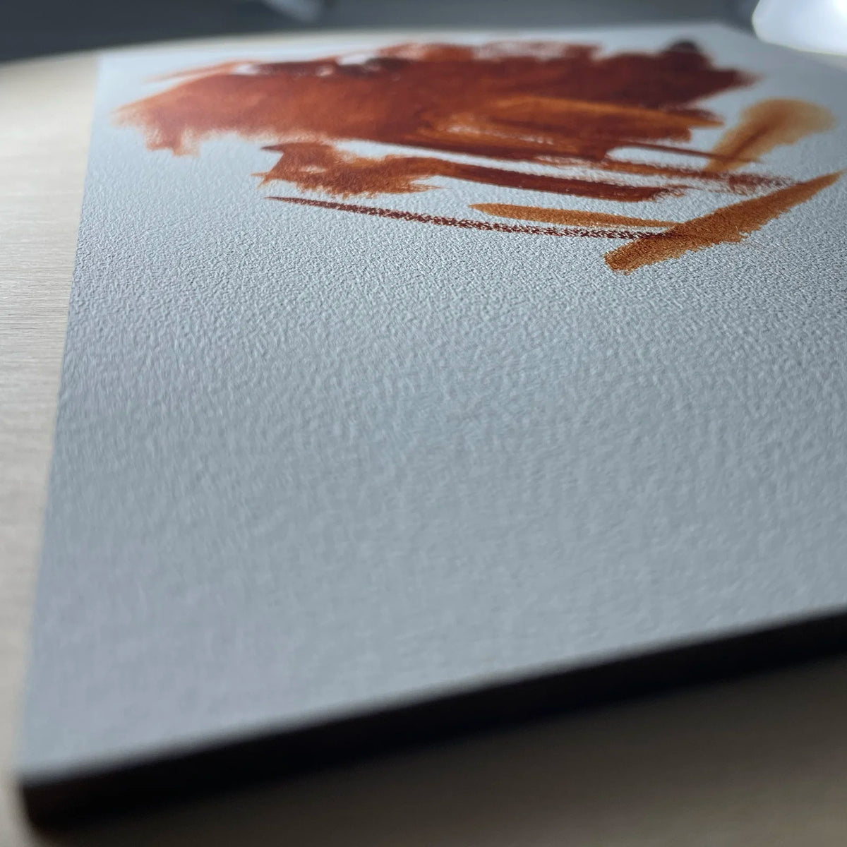 Close-up of a reddish-brown brushstroke on the textured white surface of a gesso panel.