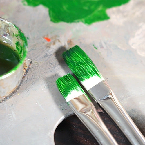 Two flat brush tips loaded with green paint above a marked white surface.