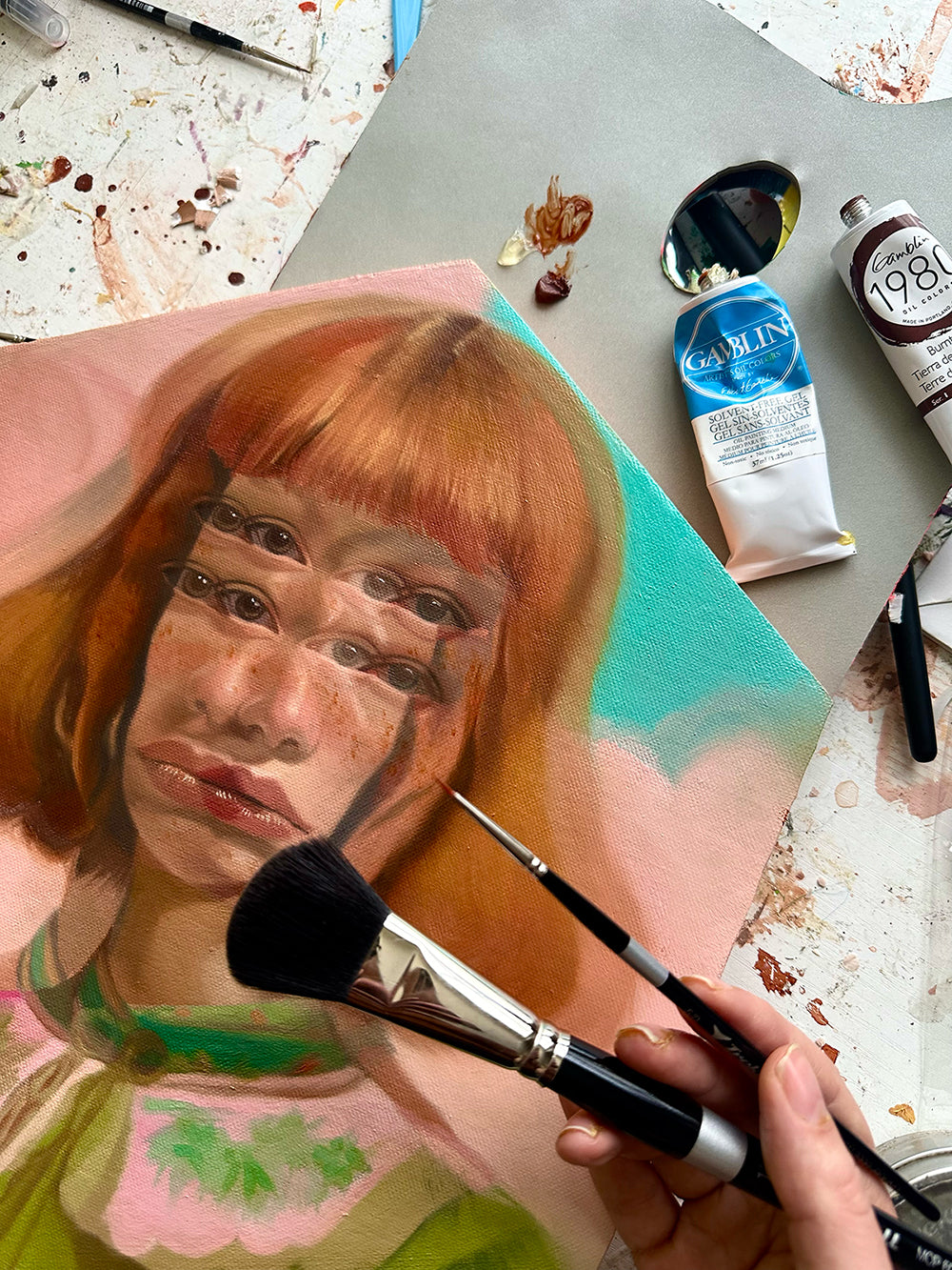 Hand holds brushes over an orange-haired woman's portrait on a round panel.