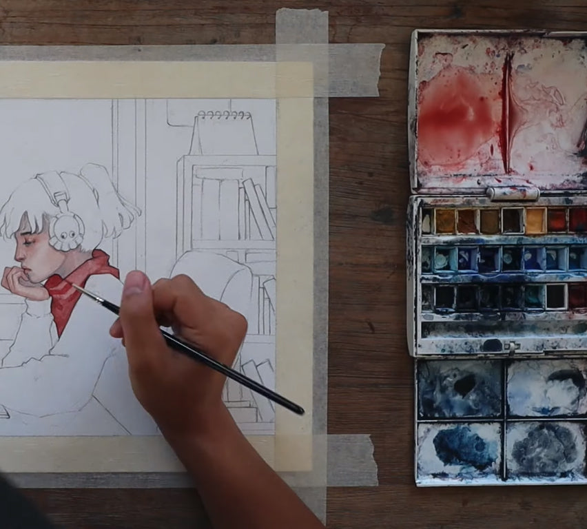 Hand paints red details in a pencil sketch beside a watercolor palette.
