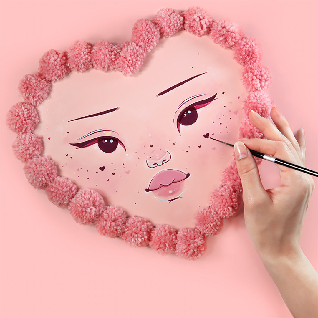 Hand paints a freckled face on a pink heart panel edged with flowers.