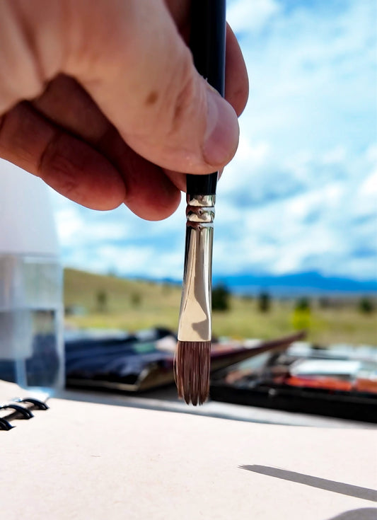 Hand dips a broad brush into a metal brush-cleaning container.