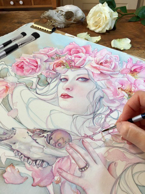 Hand paints a pale woman's face surrounded by pink flowers.