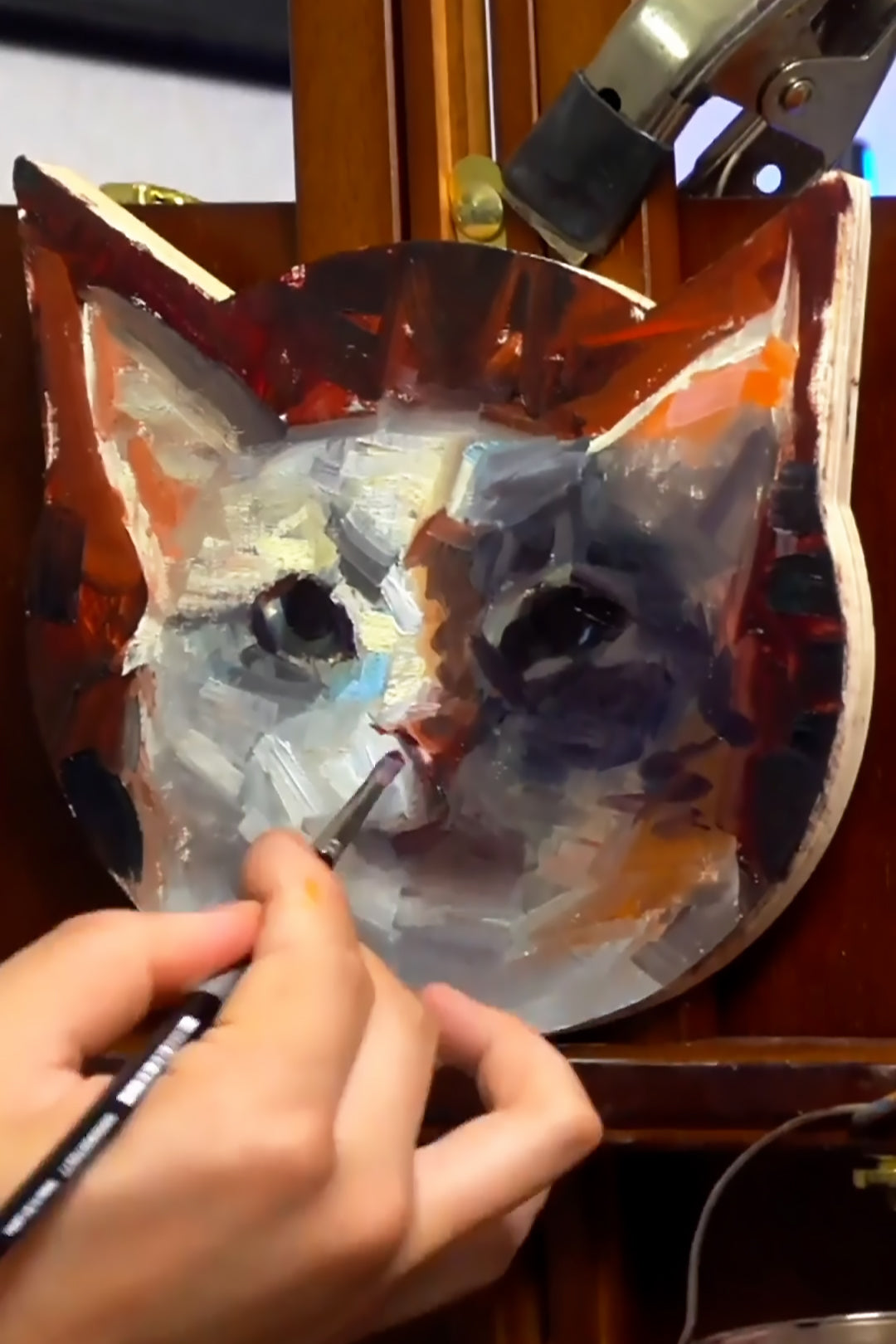 Fine brush adds detail to a gray-and-white cat portrait on a shaped panel.