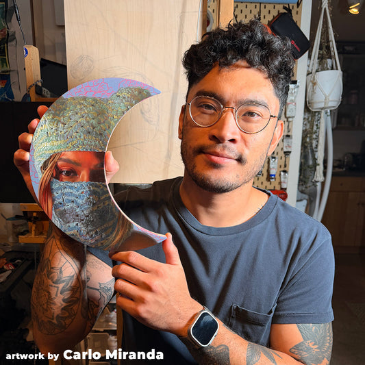 Artist with glasses holds a painted crescent panel in a studio.