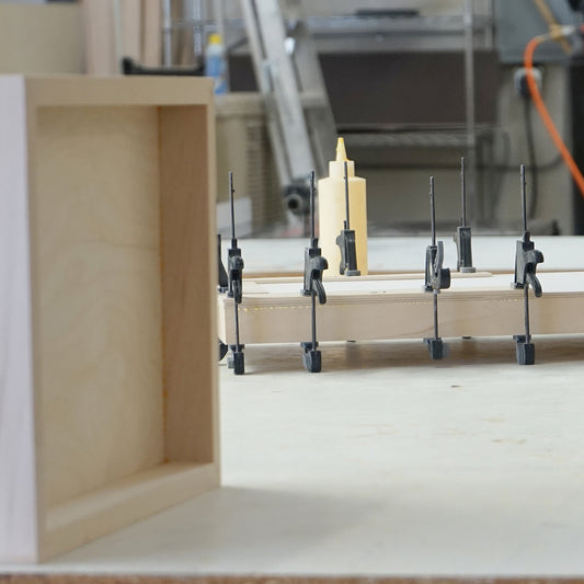 Panel-making equipment and clamps beside a pale wooden support frame.