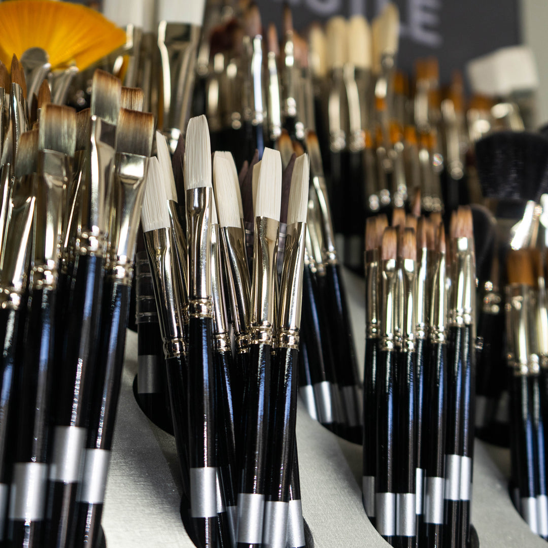 Dense arrangement of black-handled brushes with varied pale, brown and golden tips.