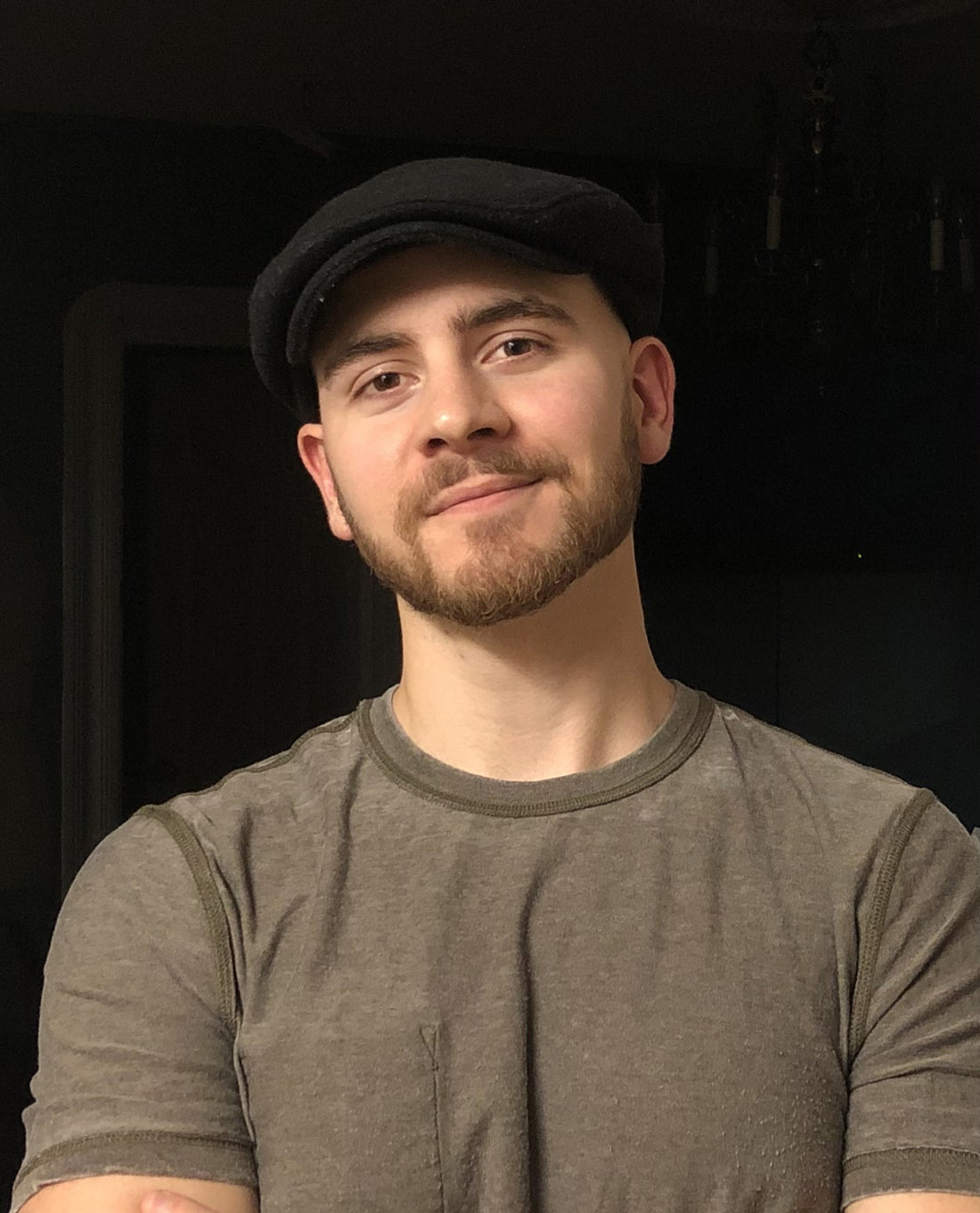Man in a dark cap and gray shirt against a dark background.
