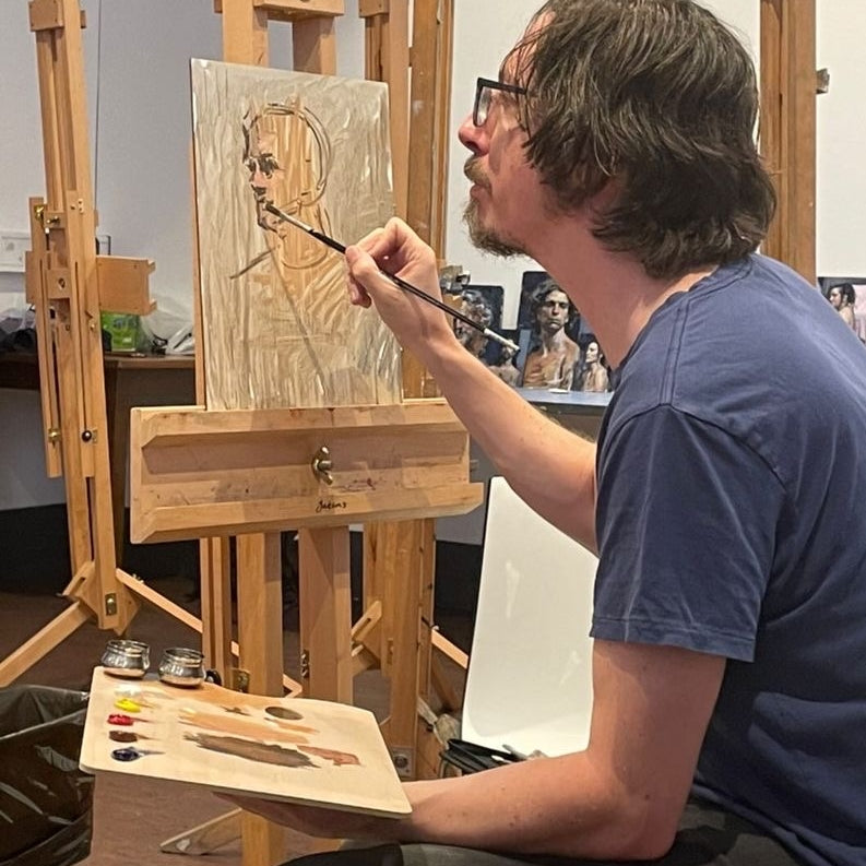Artist paints a penciled portrait on a wooden panel at an easel.