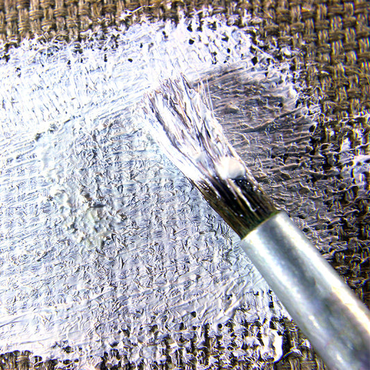 Brush spreads white coating across coarse woven fabric.