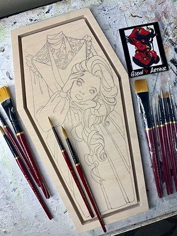 Pencil sketch on a coffin-shaped wood panel beside red-handled brushes.