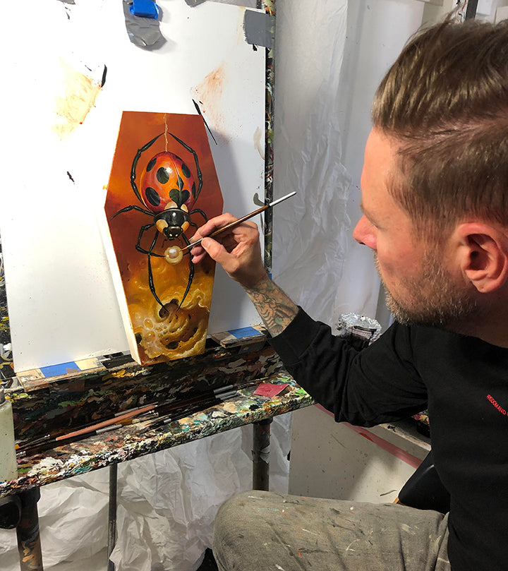 Artist paints an orange panel with a dark owl-like figure.