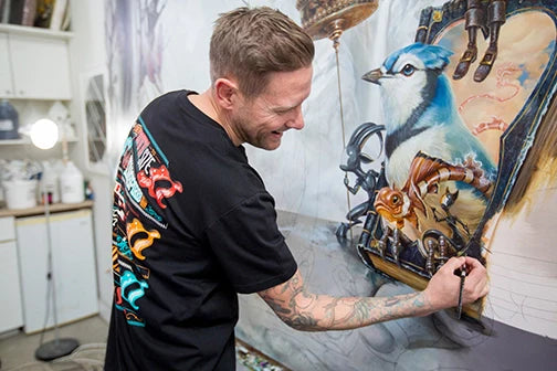 Artist paints a large surreal composition with skeletons and curled forms.