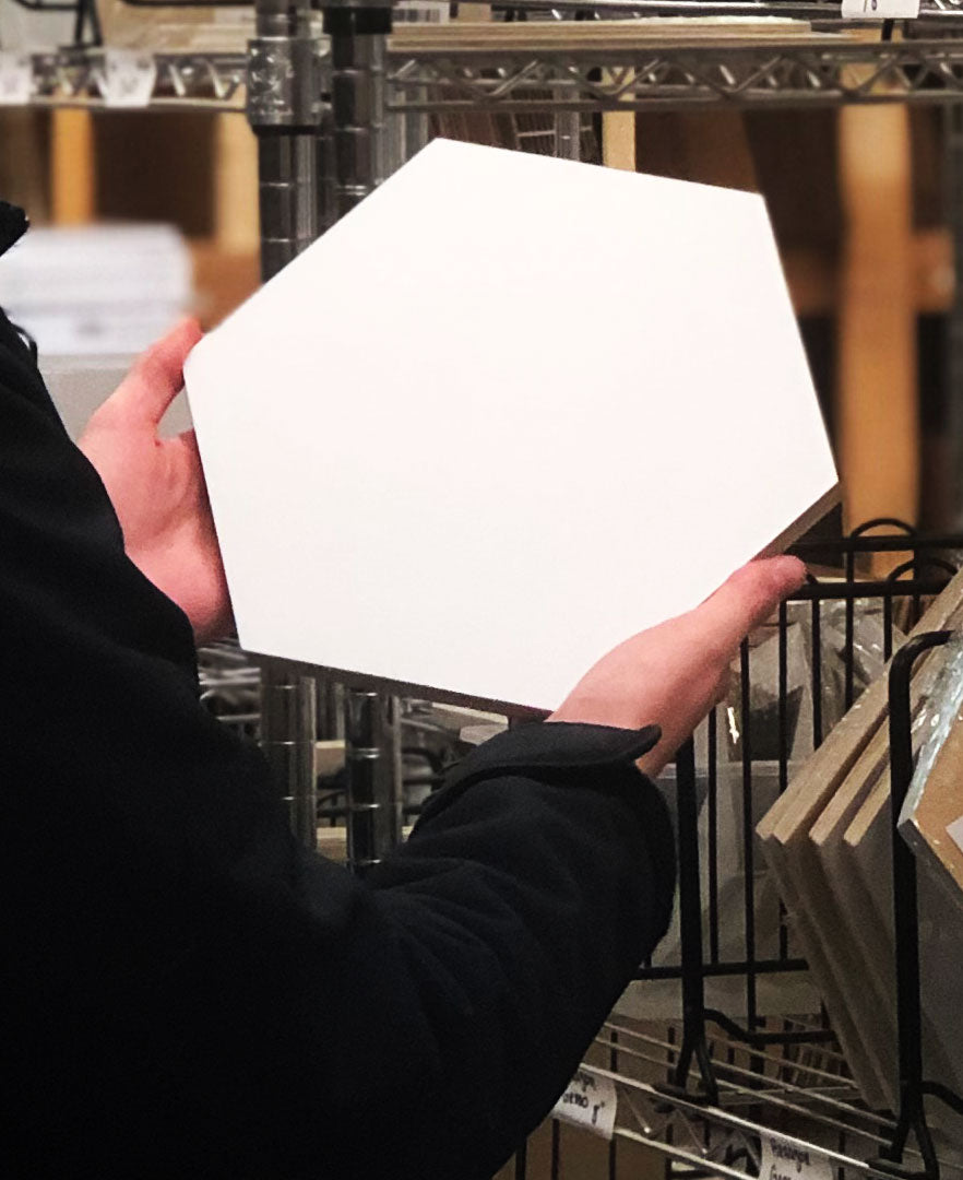 Person holds an unpainted white hexagonal panel in both hands.
