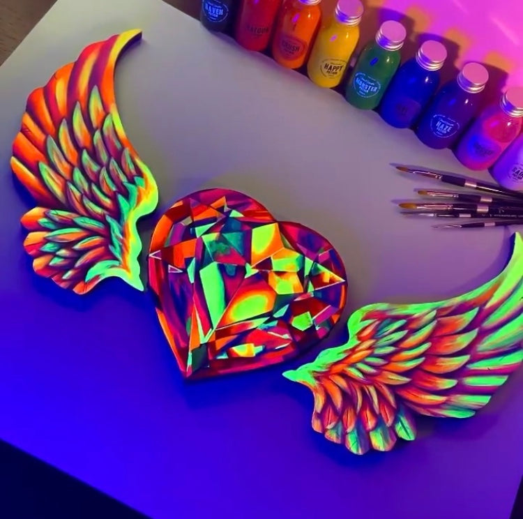 Faceted rainbow heart with spread wings beside colorful paint markers.