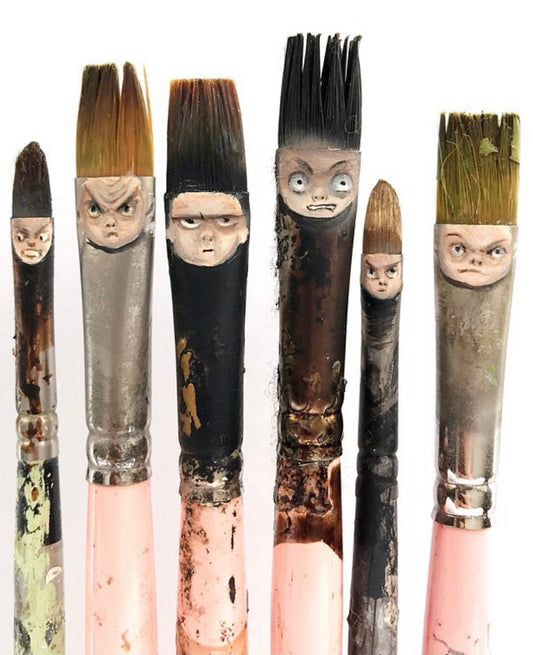 Six paintbrushes decorated with painted faces on their ferrules.