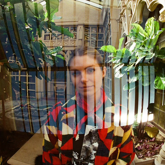 Woman seen through layered reflections of windows and greenery.