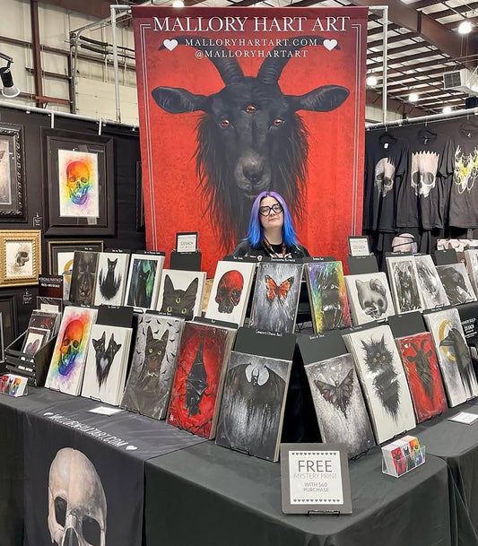 Artist beneath a large red animal banner at an art display booth.