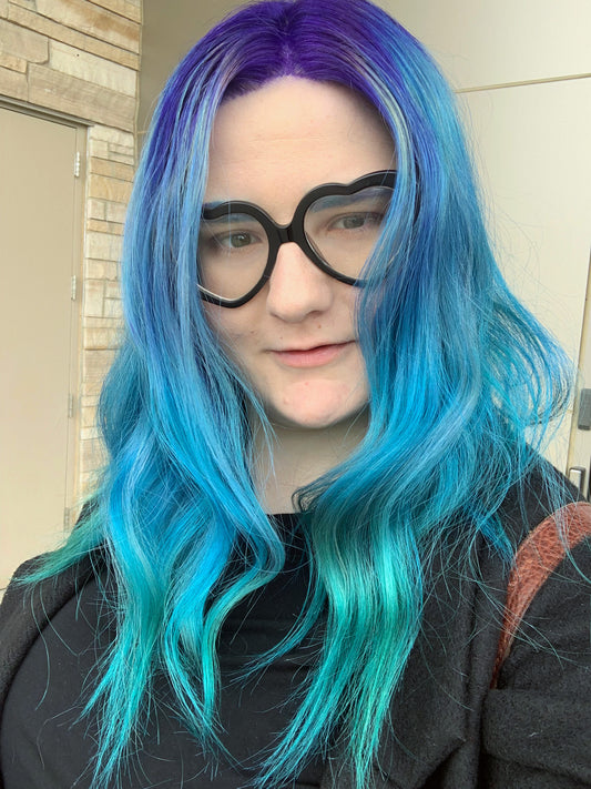 Portrait of an artist with blue-and-purple hair and black glasses.