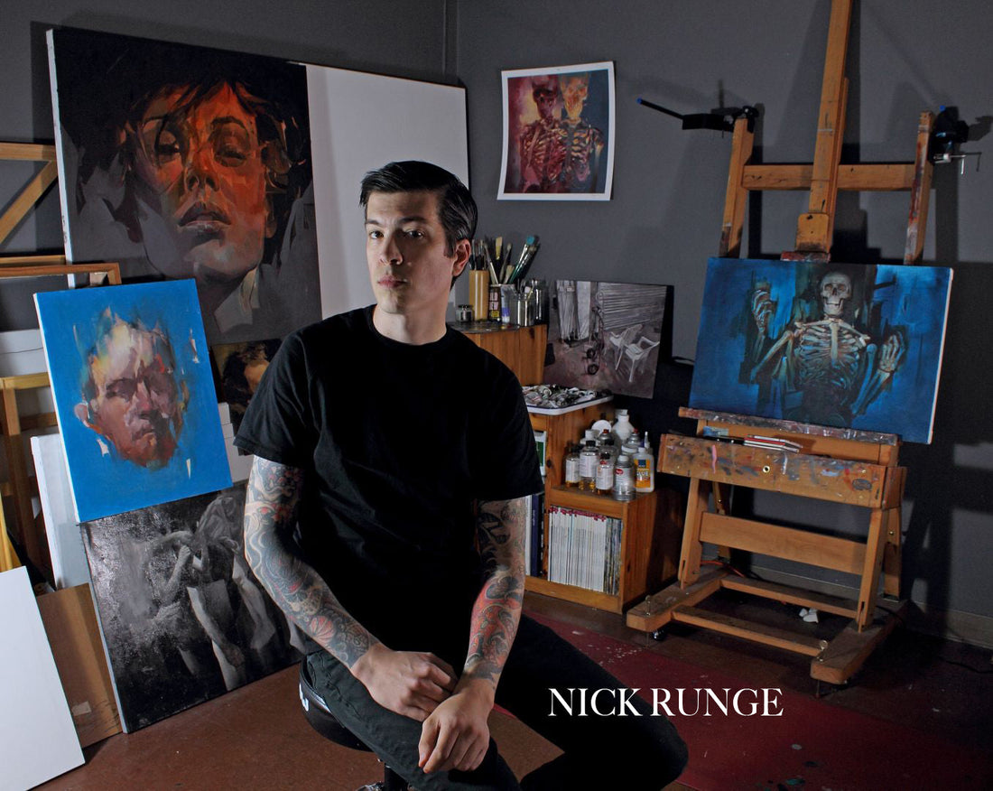 Man stands among easels and portrait paintings in a blue-walled studio.