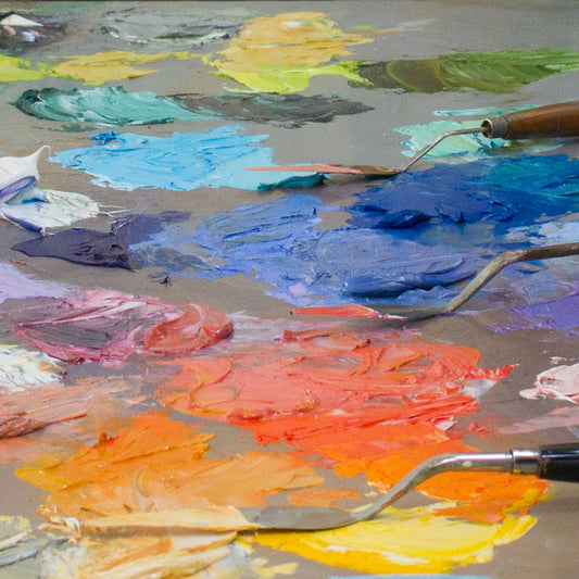 Palette knife lies among thick blue, orange, pink and yellow paint swatches.