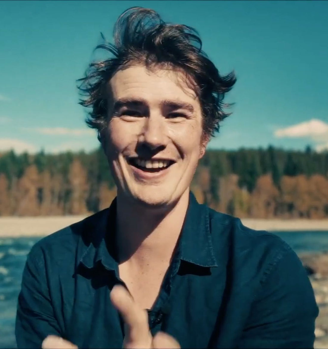 Smiling dark-haired man outdoors beneath a blue sky.