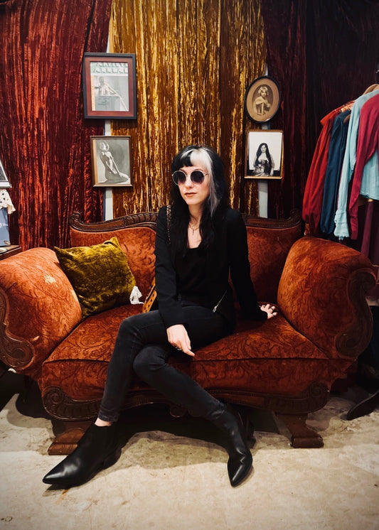 Woman in black sits on an orange couch in a room with framed artwork.