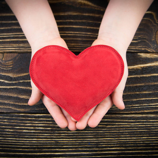 Hands hold a red heart-shaped object over a dark wooden surface.