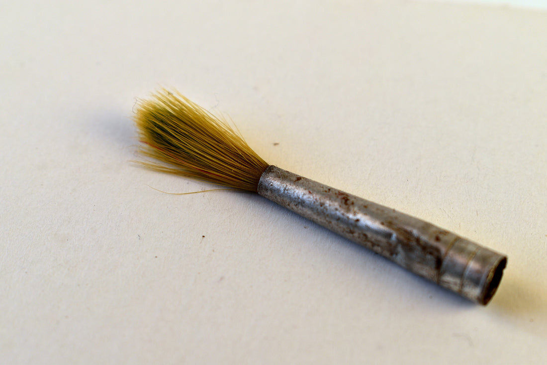 Flat brush with golden bristles lies diagonally on white.
