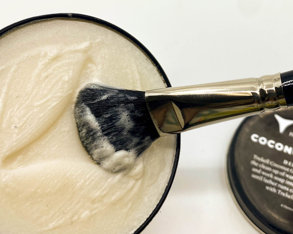 Broad brush swirls in pale coconut oil soap inside an open tin.