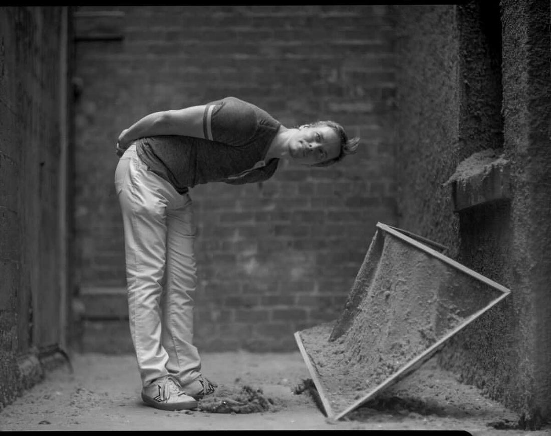 Black-and-white photograph of a person leaning over an angled panel in a brick room.