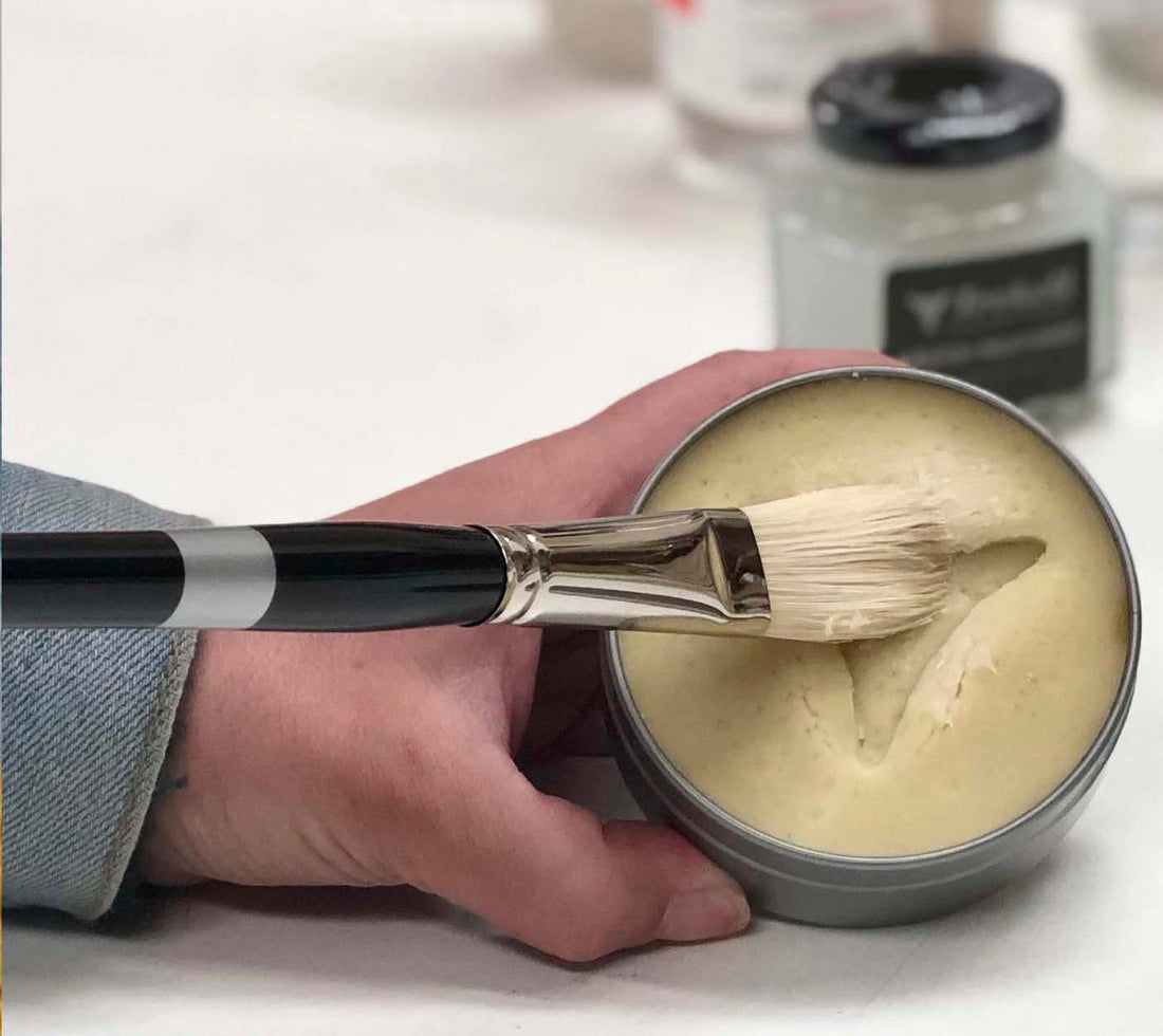 Hands hold an open soap tin while a brush presses into pale cleaner.