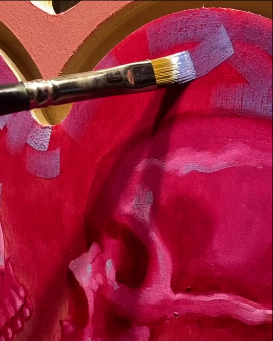 Brush sweeps pale color across bright red fabric in a painting.