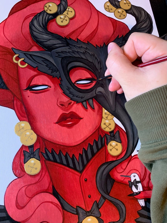 Hand paints the eye area of a red-skinned, horned woman's portrait.