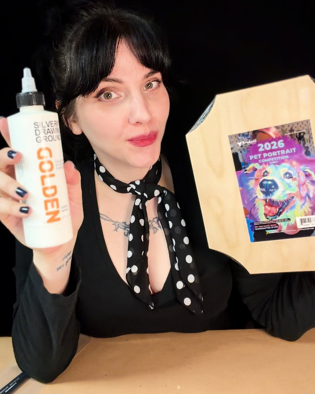 Dark-haired person holds a white bottle beside a colorful small painting.