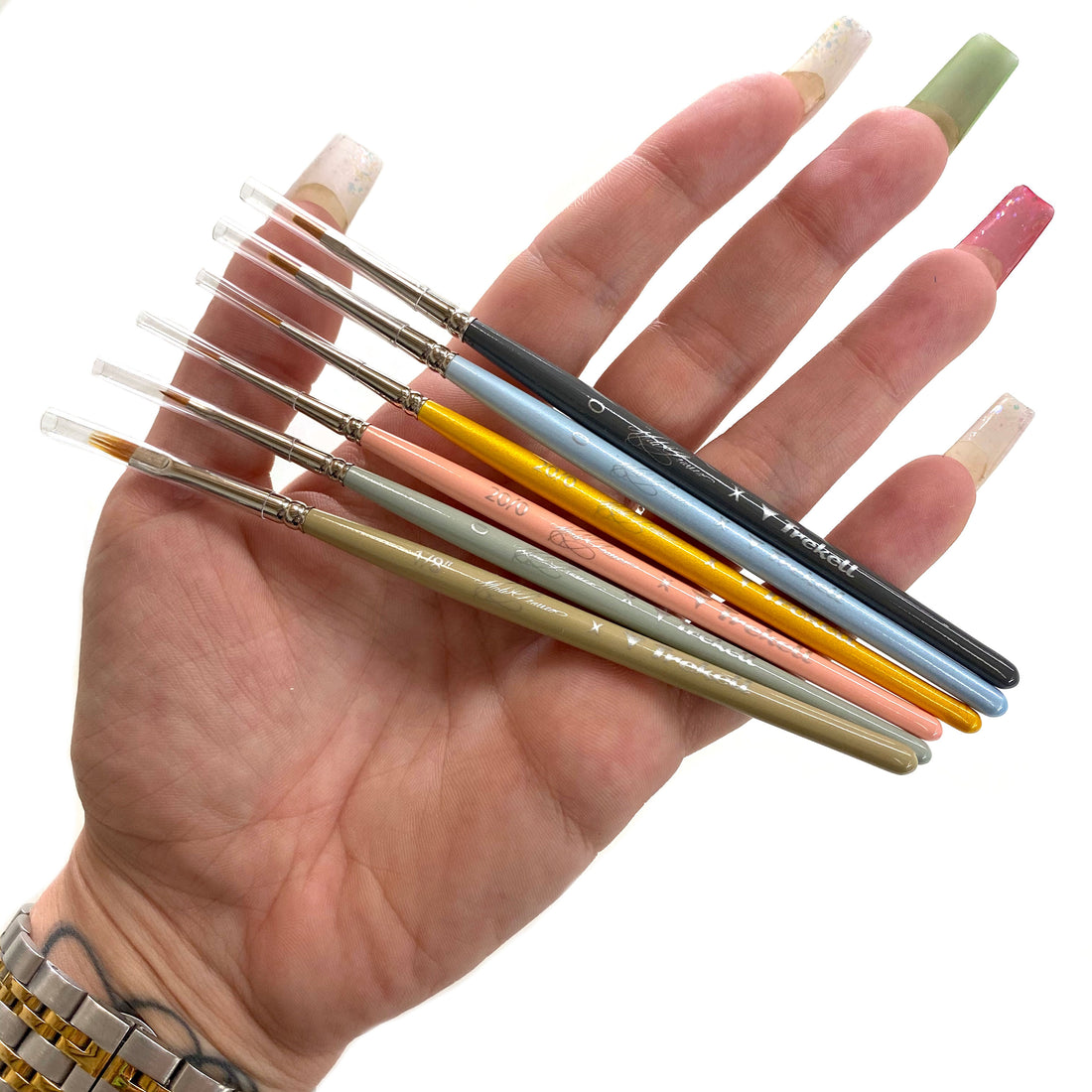 Hand holds a fan of slender colorful-handled detail brushes.