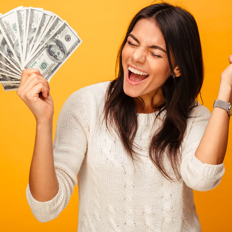 Smiling woman holds a fan of cash against yellow.