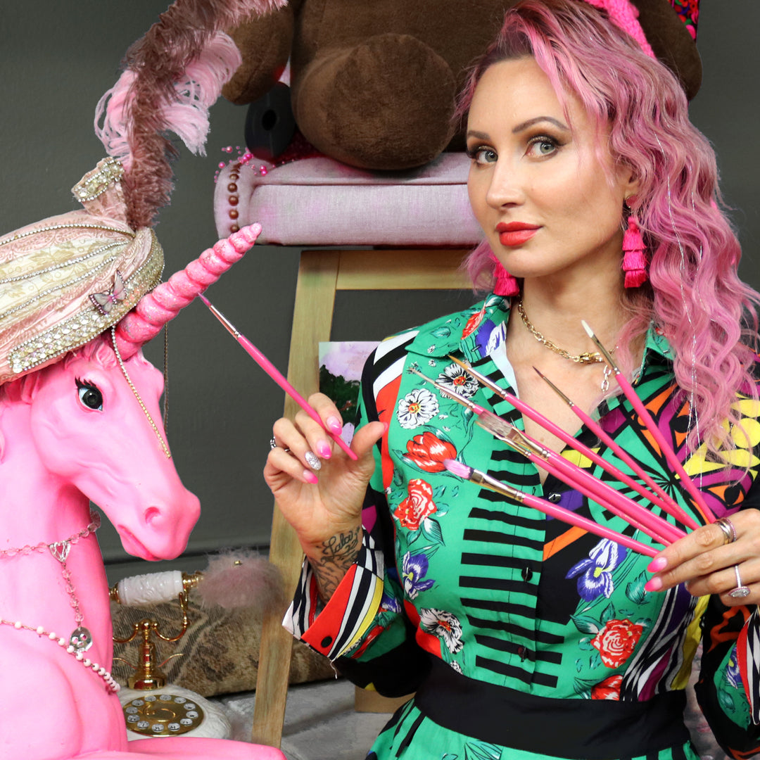 Pink-haired artist holds pink brushes beside a pink sculpted animal head.