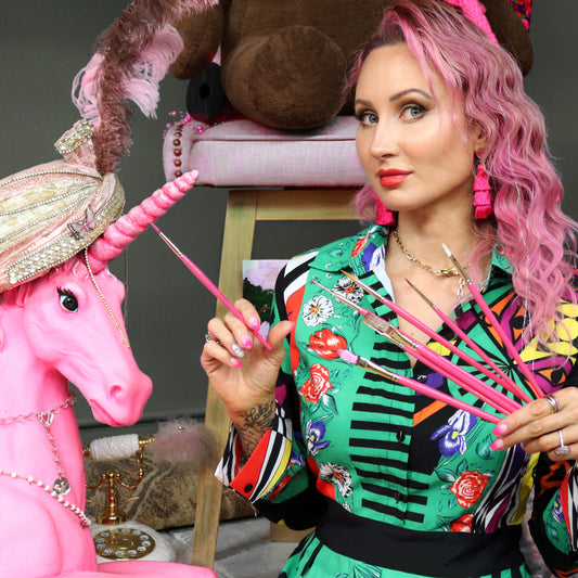 Pink-haired artist holds pink brushes beside a pink sculpted animal head.