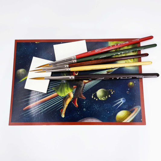 Several brushes rest across a small colorful painting with a red border.