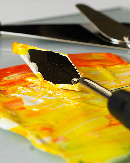Palette knife lifts yellow paint from an orange-and-yellow palette.