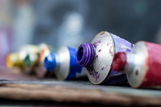 Paint-covered tubes with colored caps arranged on a wooden table.