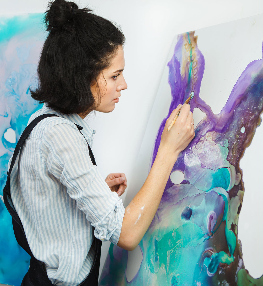 Artist paints purple and turquoise shapes on a large canvas.