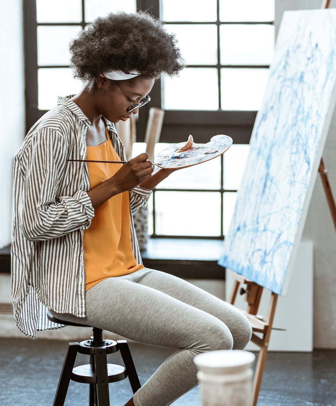 Artist checks a smartphone while standing beside a canvas.