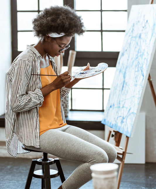 Artist checks a smartphone while standing beside a canvas.