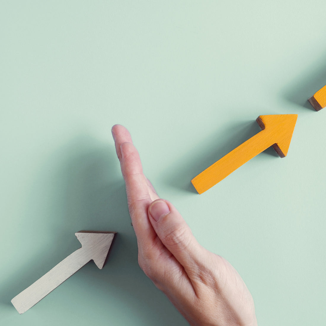 Hand blocks a gray arrow while an orange arrow rises diagonally.