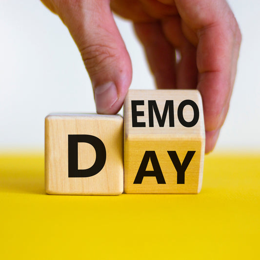 Hand arranges letter blocks to read Demo Day on yellow.
