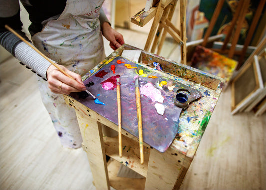 Artist holds a paint-covered wooden palette with assorted brushes.